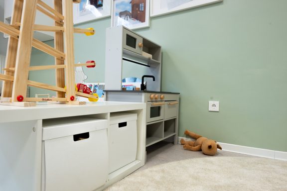 Spielküche in einem Raum mit Spielzeug und einem Teddybären auf dem Boden.