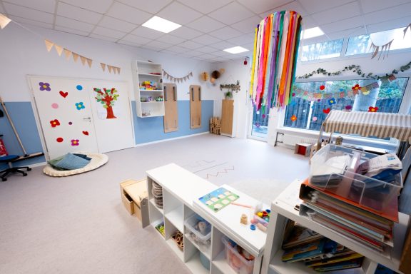 Helle, offene Kita-Räumlichkeit mit Spielbereichen und bunten Dekorationen.